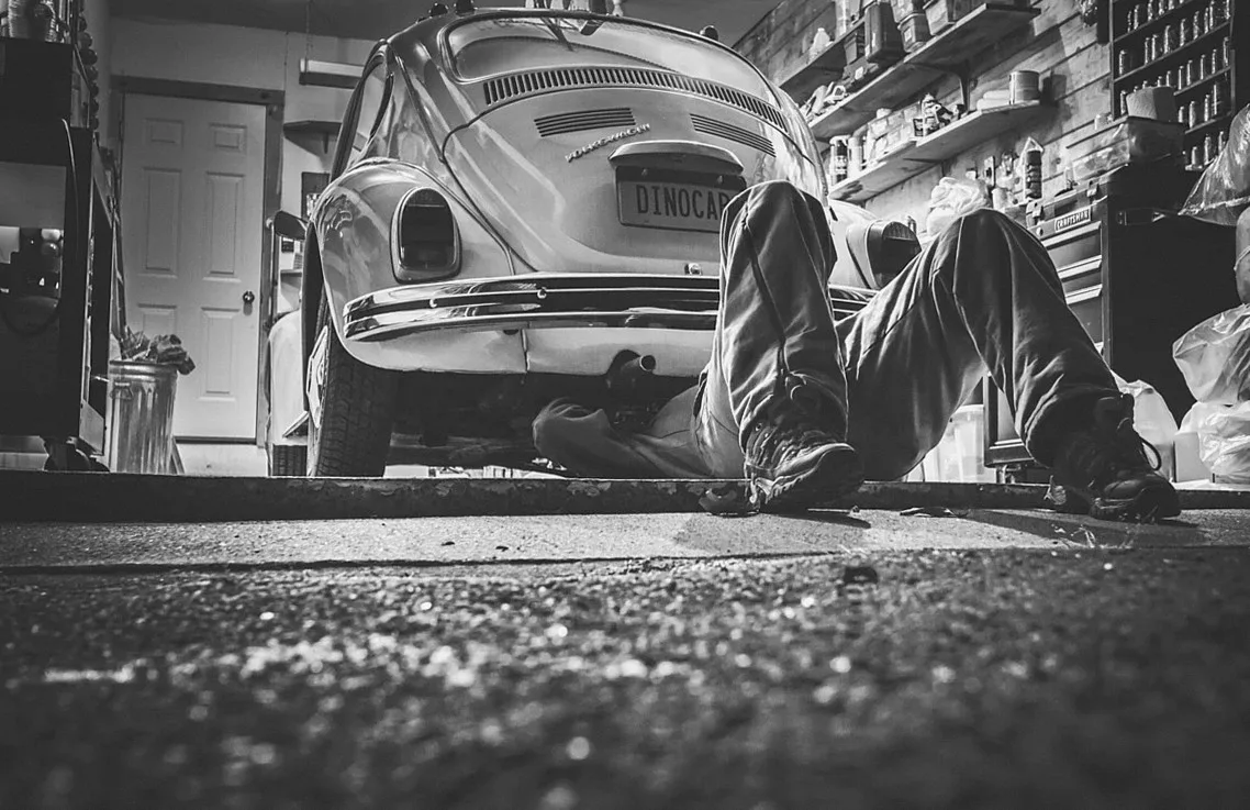 古い車の下に入って作業する人のモノクロ写真
